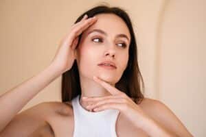 Woman gently touching her face, considering the benefits of a mini brow lift.