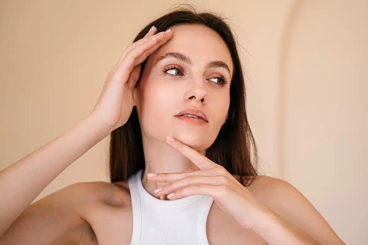 Woman gently touching her face, considering the benefits of a mini brow lift.