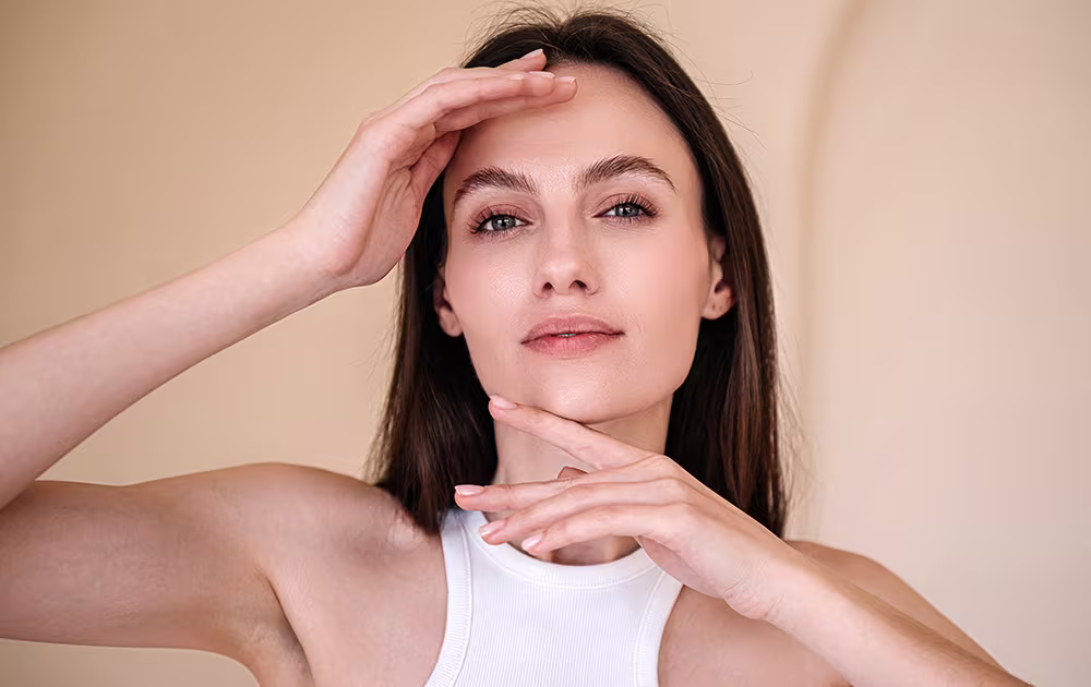 Woman gently touching her face, considering the benefits of a mini brow lift.