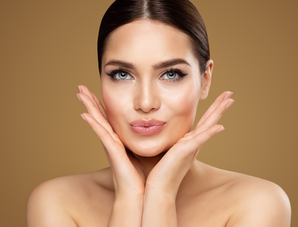 Woman with hands framing her face, showing smooth, youthful skin, illustrating the benefits of dermal fillers for enhancing facial contours and natural beauty.