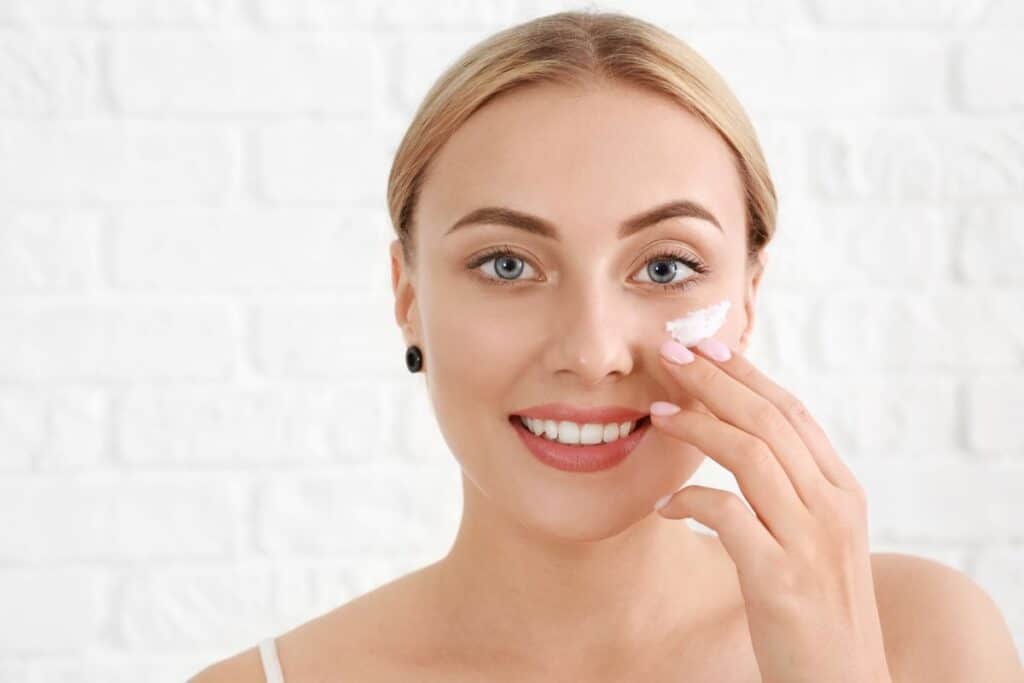 Woman smiling and applying sunscreen to her face, focusing on a healing scar.