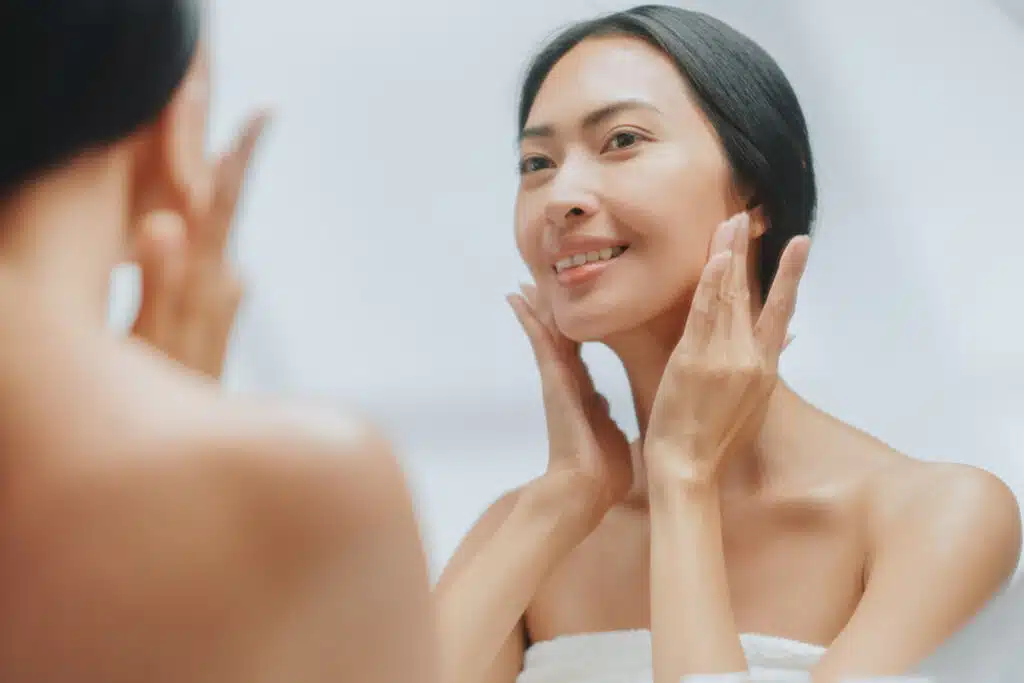 Woman examines her face in the mirror, noting early Botox benefits on the face.