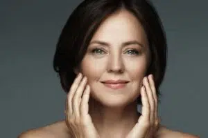 Smiling woman touching her face, showing defined upper lip and harmonious facial balance after lip lift surgery.