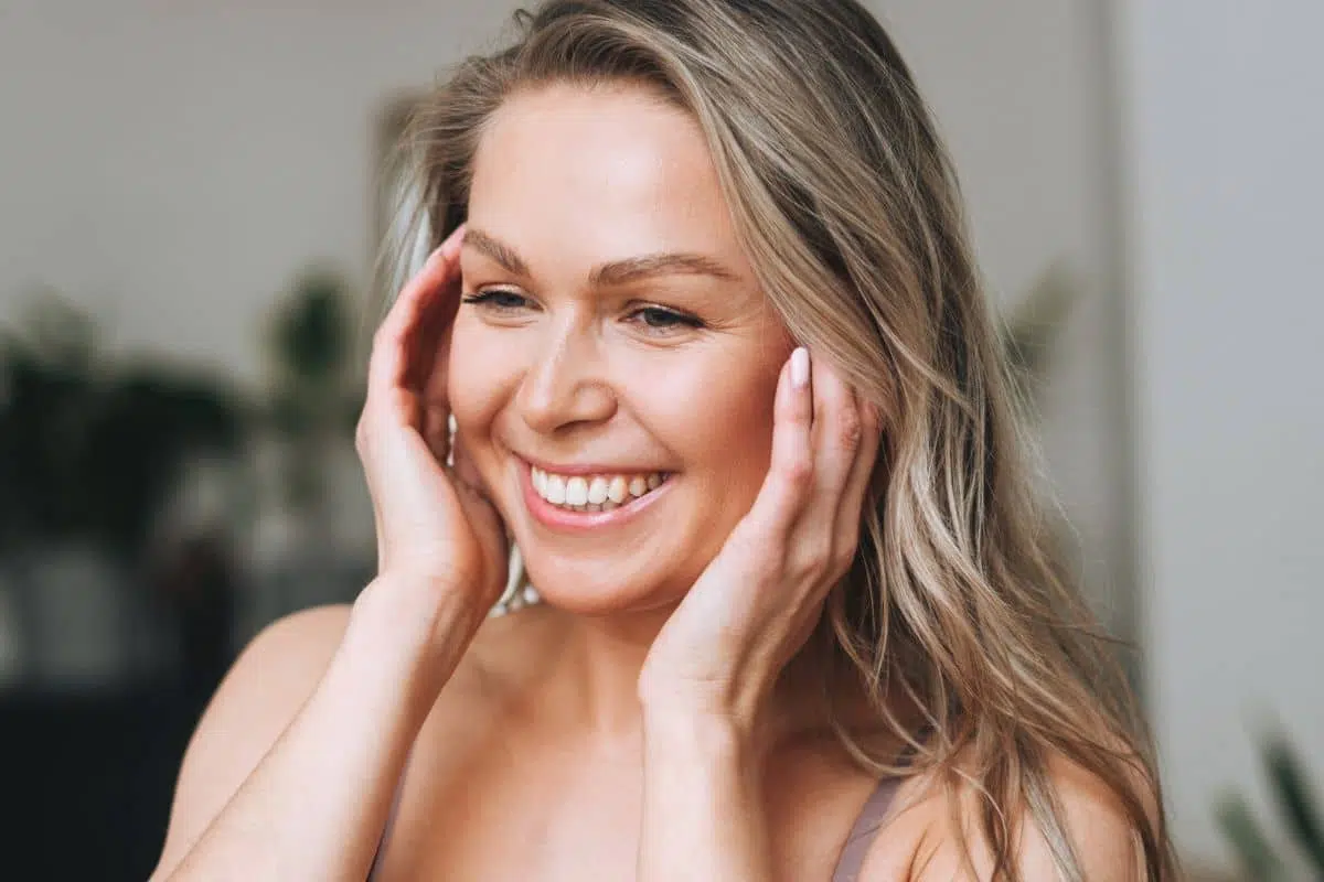 Happy woman touching her face, showcasing natural and youthful appearance after undergoing a mini facelift procedure.