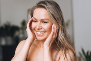 Happy woman touching her face, showcasing natural and youthful appearance after undergoing a mini facelift procedure.