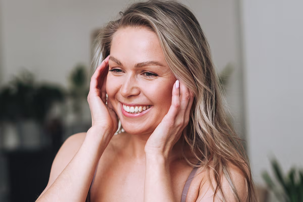 Happy woman touching her face, showcasing natural and youthful appearance after undergoing a mini facelift procedure.