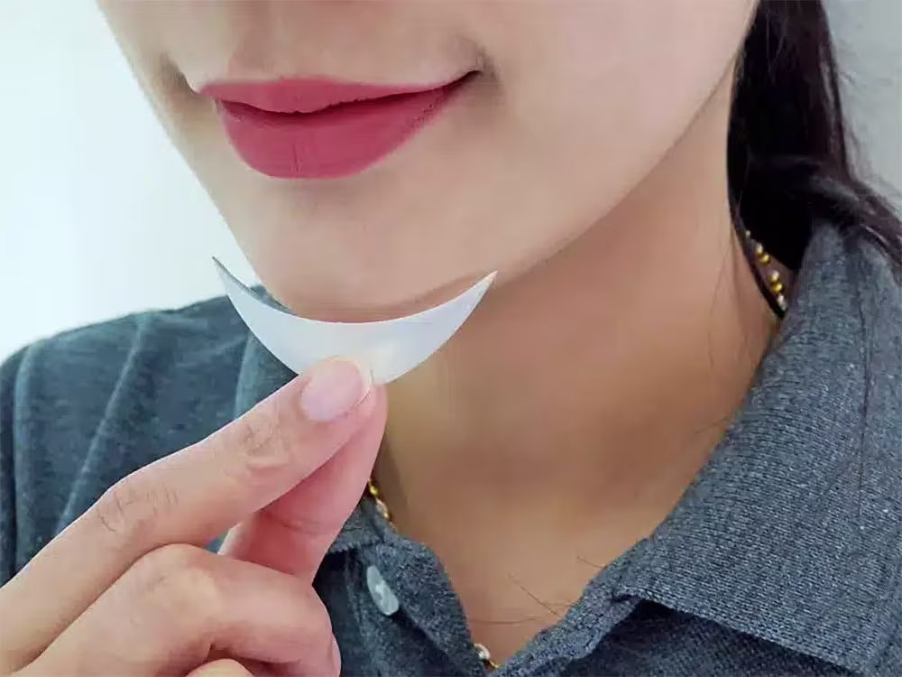 Woman holding a silicone chin implant under her jawline before undergoing a chin augmentation procedure