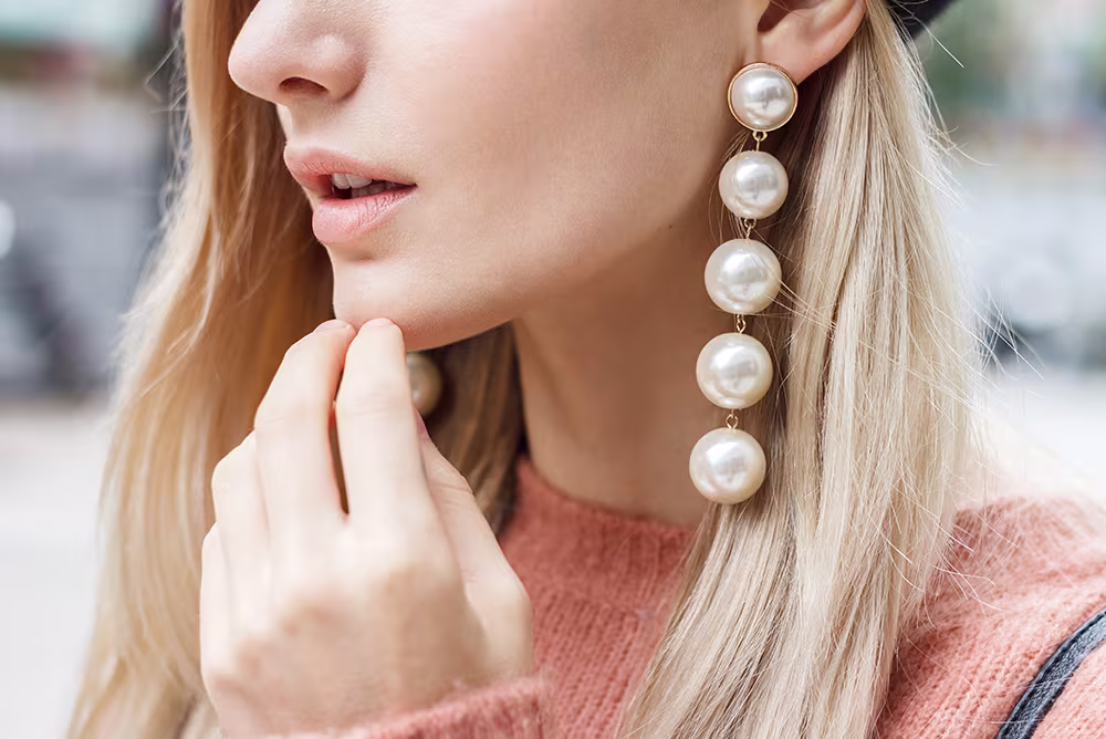 Close-up of woman wearing large pearl earrings, showing stretched earlobes from prolonged heavy earring use