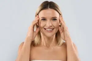 Woman smiling and gently touching temples, representing preparation and confidence before blepharoplasty surgery.