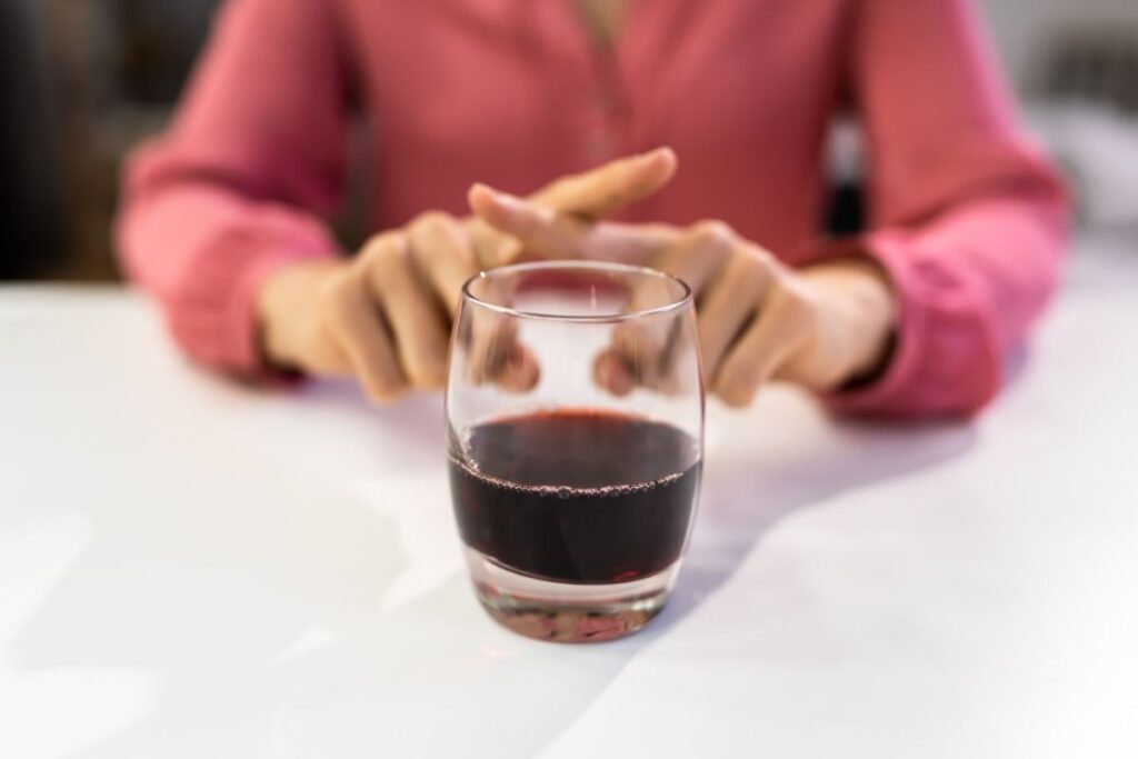 Close-up of woman in pink shirt avoiding a glass of red wine before blepharoplasty surgery for safe recovery.