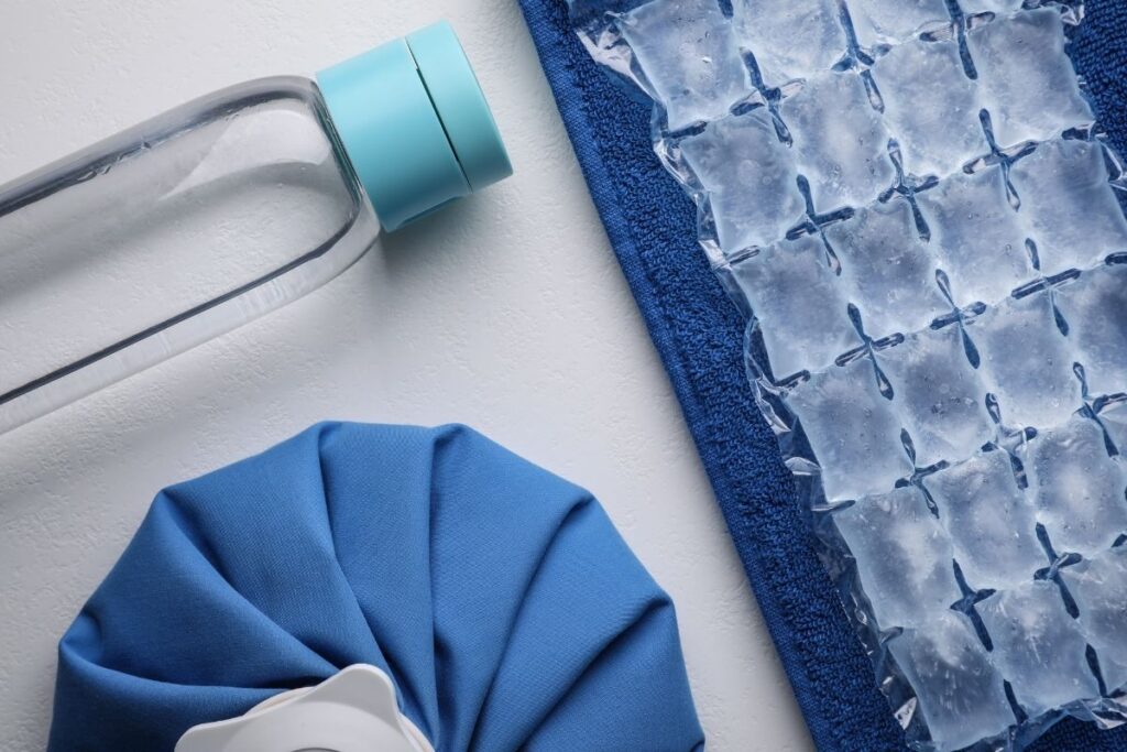 Recovery essentials including water bottle, ice packs, and compresses for post-eyelid surgery home care setup.