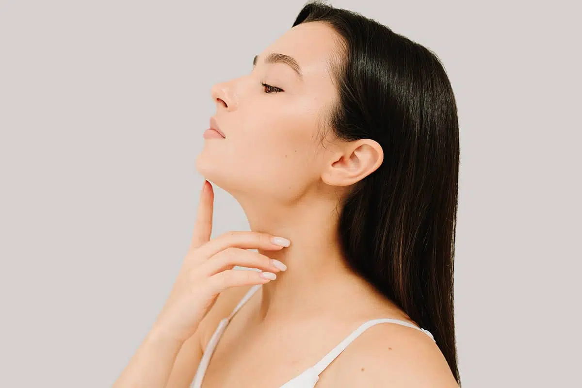 A profile view of a woman with long dark hair tilting her chin up and gently placing her finger along her well-defined jawline.